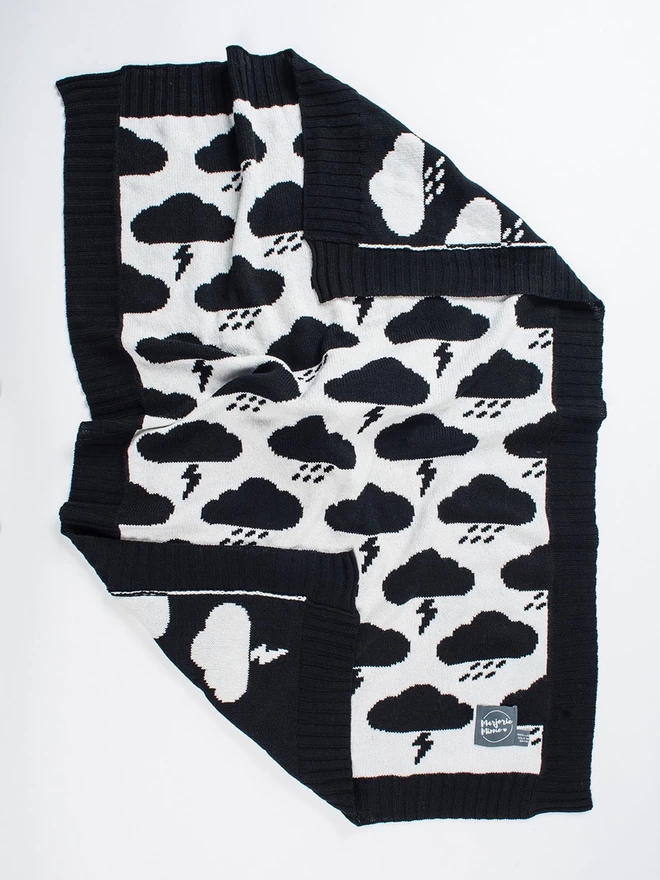 A baby blanket with black storm clouds pattern laid out flat with the corners ruffled and flipped over to show the reverse colour way.