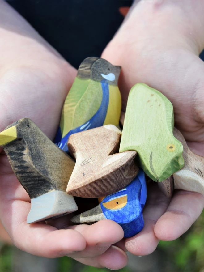 a collection of wooden toy birds and animals in a childs hands