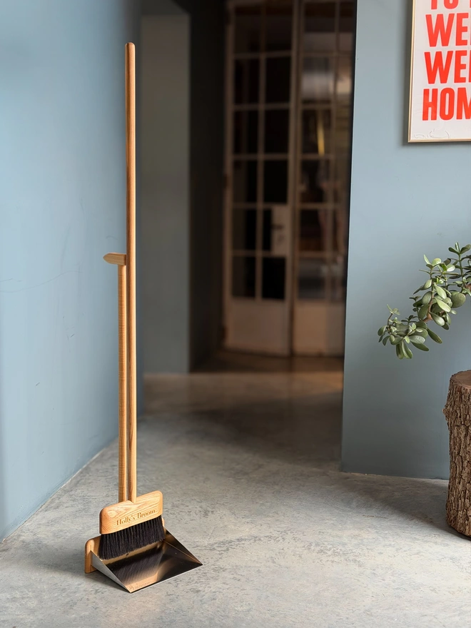 Personalised standing dustpan and broom set with oiled wood handles, in a hallway
