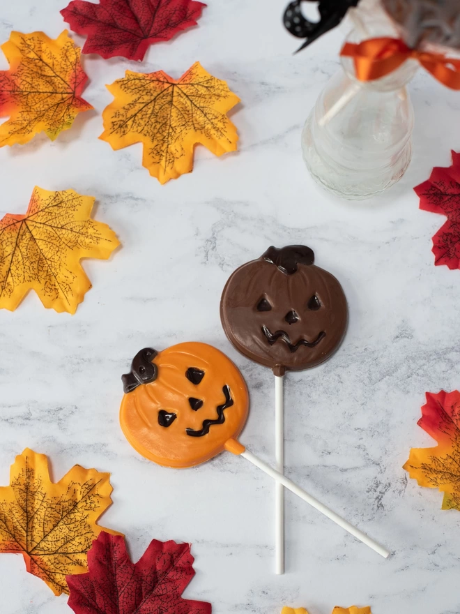 Orange and milk chocolate pumpkin lollipops surrounded by leaves