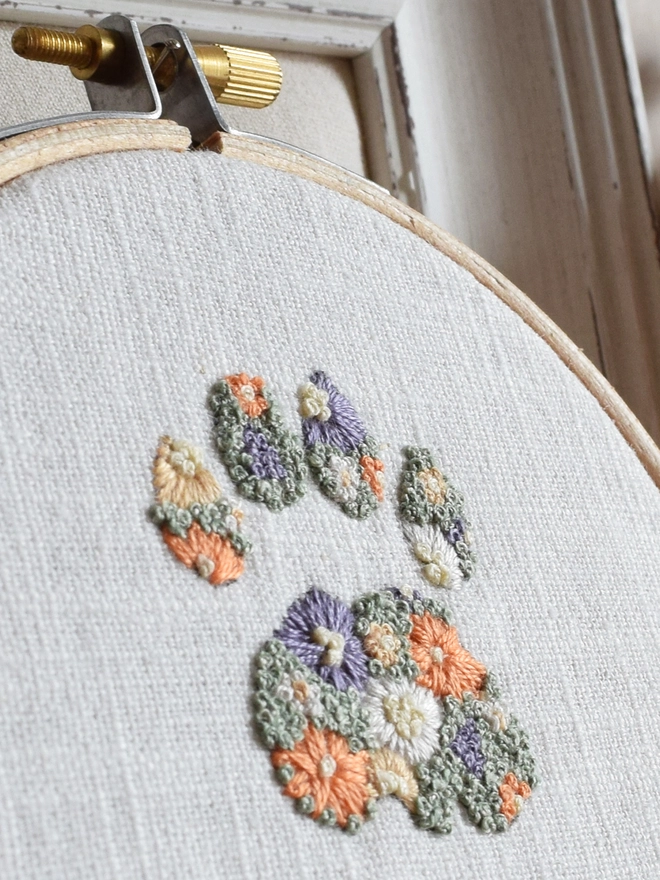 An embroidered Cats Paw of Golden Yellows and Bright Orange Blossoms with Green French Knot grass background.  