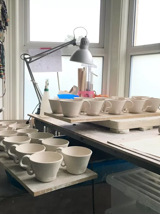 20 fresfly made porcelain cups on two wareboards ,in front of a window with a desk lamp