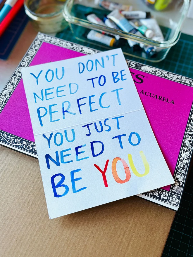 A handwritten note in watercolour on 300gsm recycled scrap card that reads "You Don't Need To Be Perfect You Just Need To Be You"