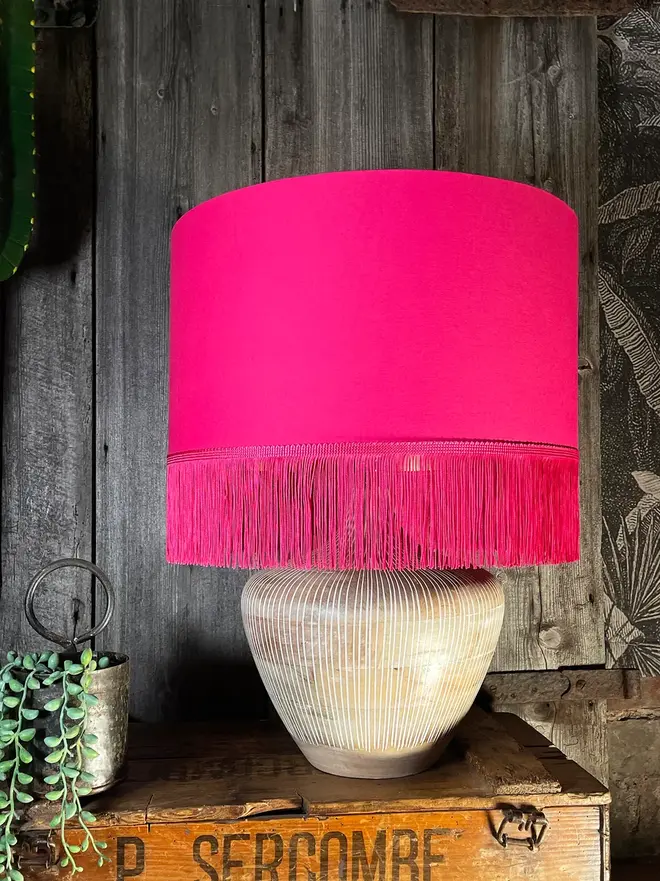 Pomegranate Pink Lampshade With Gold Lining & Pink Fringing, on a table. 