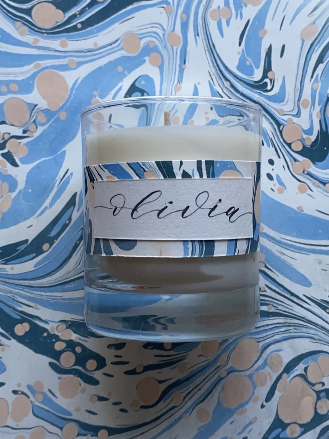 Hand Poured Scented Candle With Personalised Marbled Label seen on marble paper.