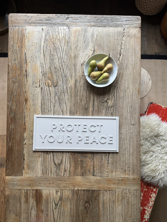 a white sign on a rustic table that says protect your peace with a bowl of pears 