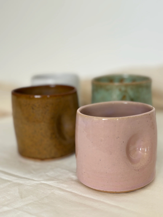 Pinch Mug. Four Regular mugs, Pink, Shoreline, Green, White, against a white and cream background.