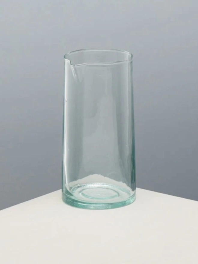Glass Carafe, a large glass jug sitting on a plain counter top against a baby blue backdrop. 