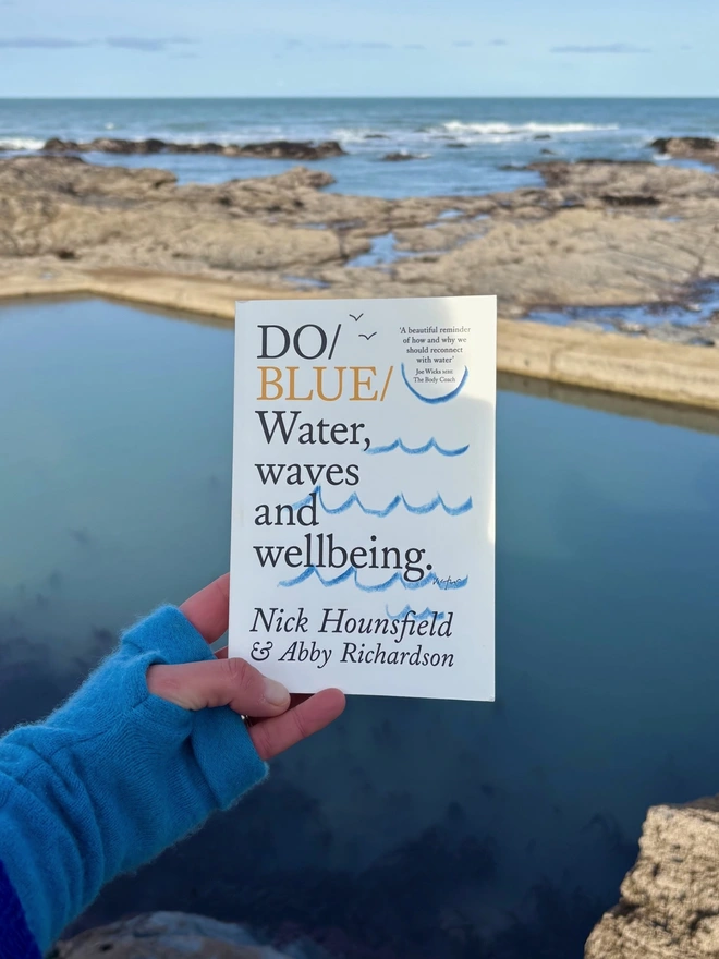 Book held up in front of body of water and blue sky