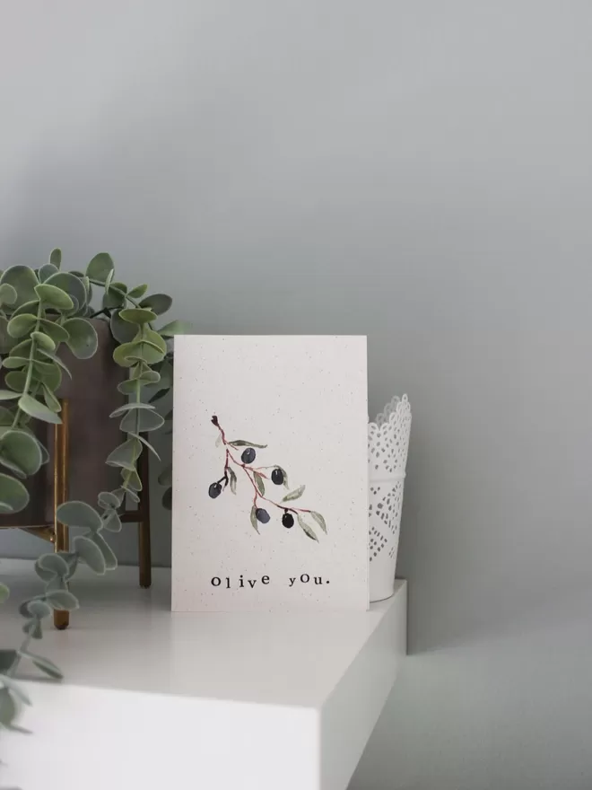'Olive You' card being displayed on shelf with potted plant