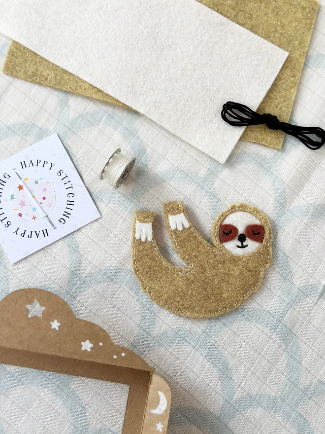 A handmade sloth finger puppet lays beside the craft kit components to make it.