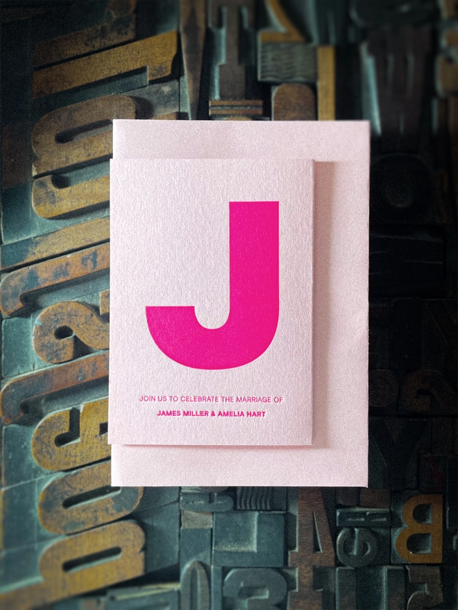 Bespoke Amour concertina wedding invitation unfolded to reveal oversized initials, heart motif and personalised wedding details, hand printed in fluorescent pink on luxury Candy Pink card.