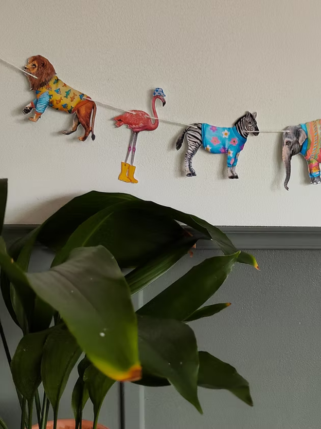 safari animals paper garland. bunting featuring illustrated animals in party outfits hung on a wall.