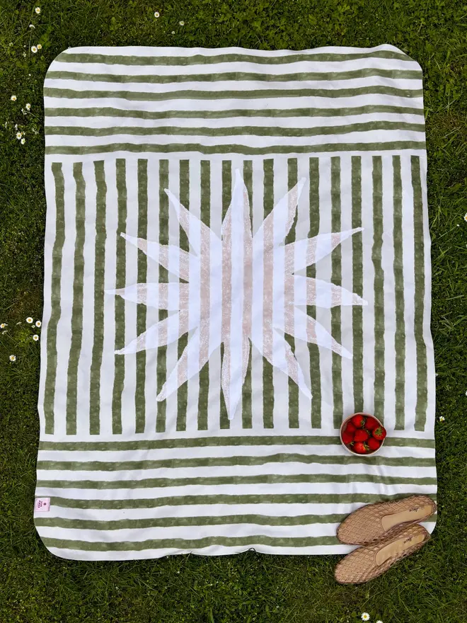 sun stripe fleece blanket. a green and white striped picnic blanket on grass.