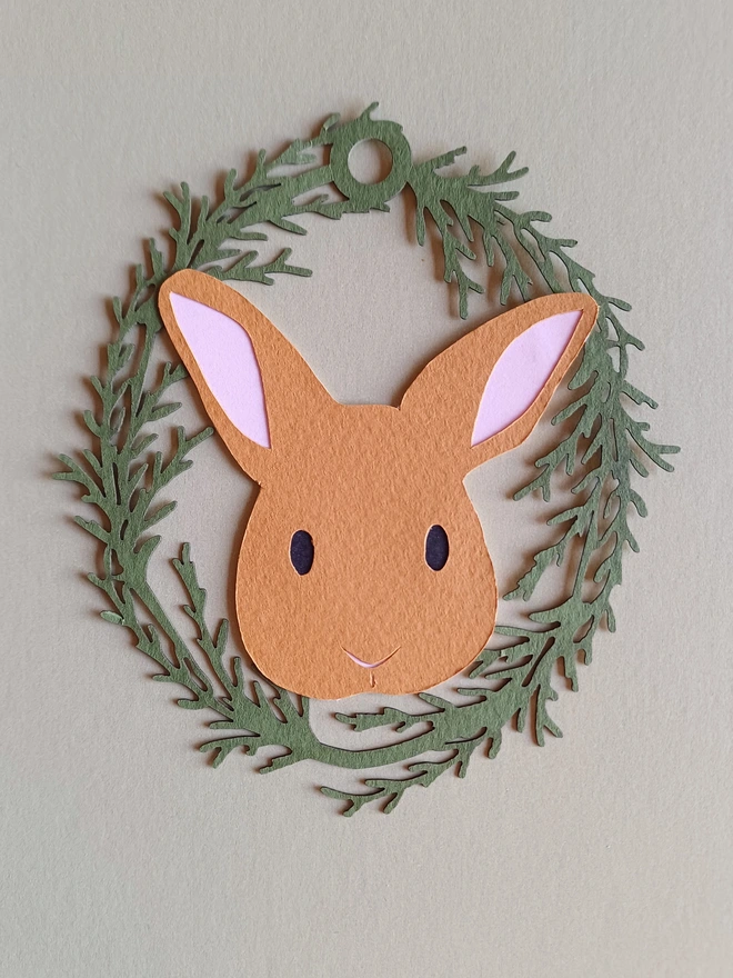 Black Bunny Easter Tree Decoration. Toffee brown bunny face with black eyes and pale pink ears inside olive green foliage wreath oval