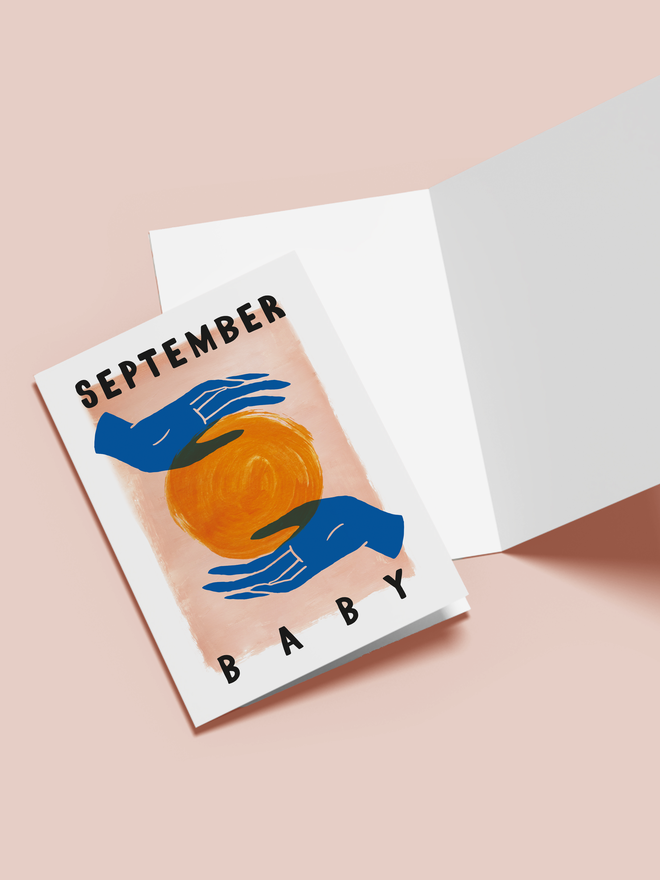 september baby illustrated card. a pink card with the sun held between two blue hands.