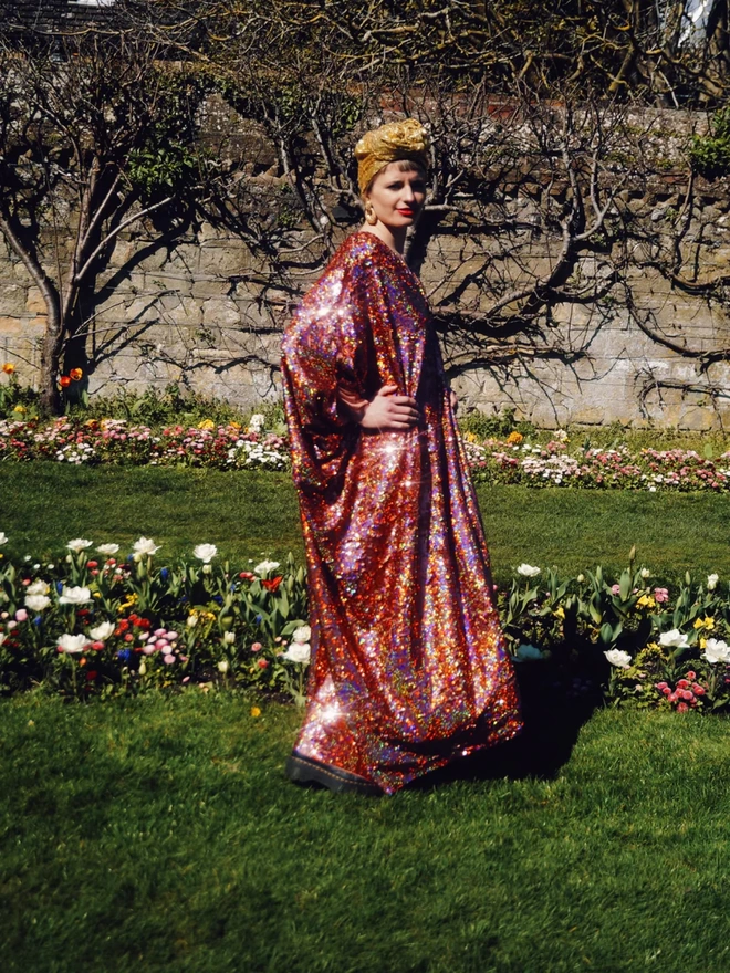 Rose Gold Holographic Sequin V-neck Kaftan Gown seen on a woman walking through a garden.