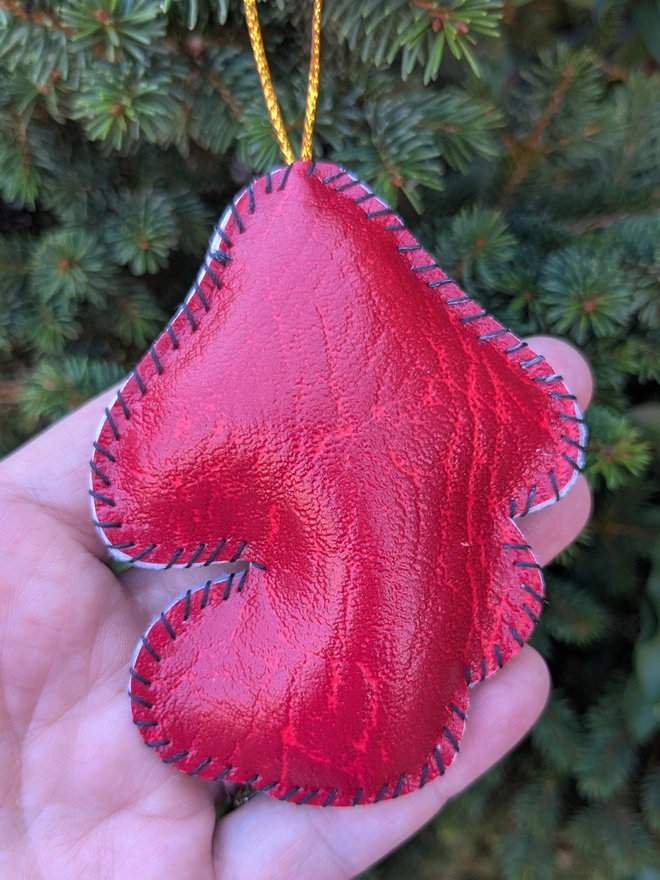 The red reverse of hand stitched personalised toadstool Christmas decoration made from vegan-friendly faux leather, featuring a red mushroom cap, holly details and a personalised name banner.