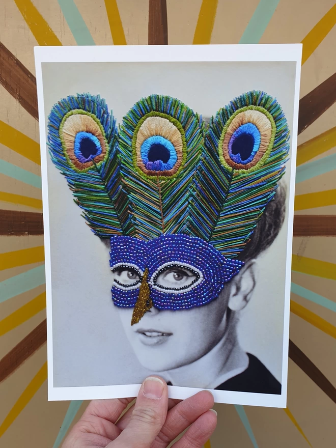 Black and white photograph print, woman wearing embroidered peacock mask held against wall