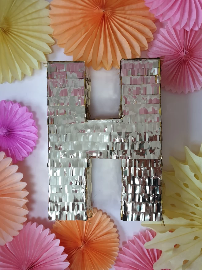 Metallic letter H pinata surrounded by soft pastel paper fans