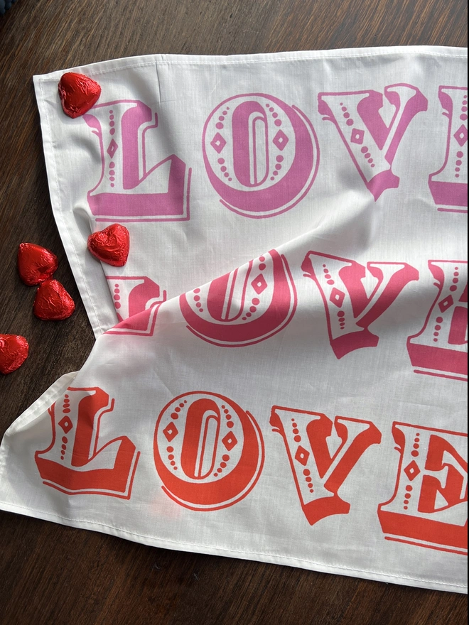 LOVE LOVE LOVE printed cotton Valentines handkerchief on a table with red heart chocolates