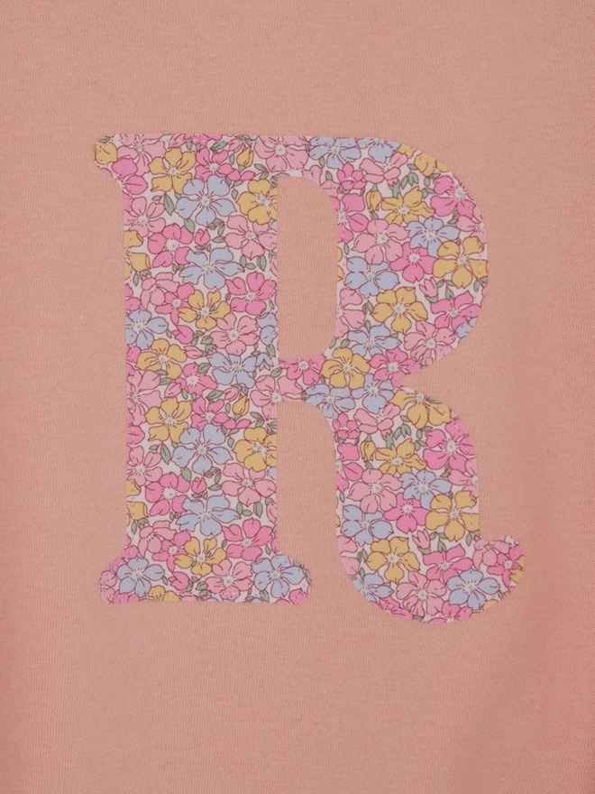 a personalised dusty pink sweatshirt with her initial sewn on the front in floral liberty point, a close up of the appliqué stitching