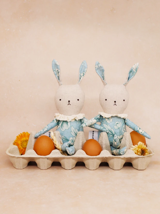 Handmade rabbit dolls with blue floral fabric and off-white ruffle collar. A white tag with the brand name ‘BOKUNO’ is sewn on the side.
