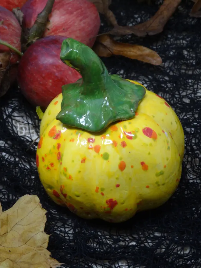 A ceramic decorative pumpkin in yellow spotted glaze with a green stem