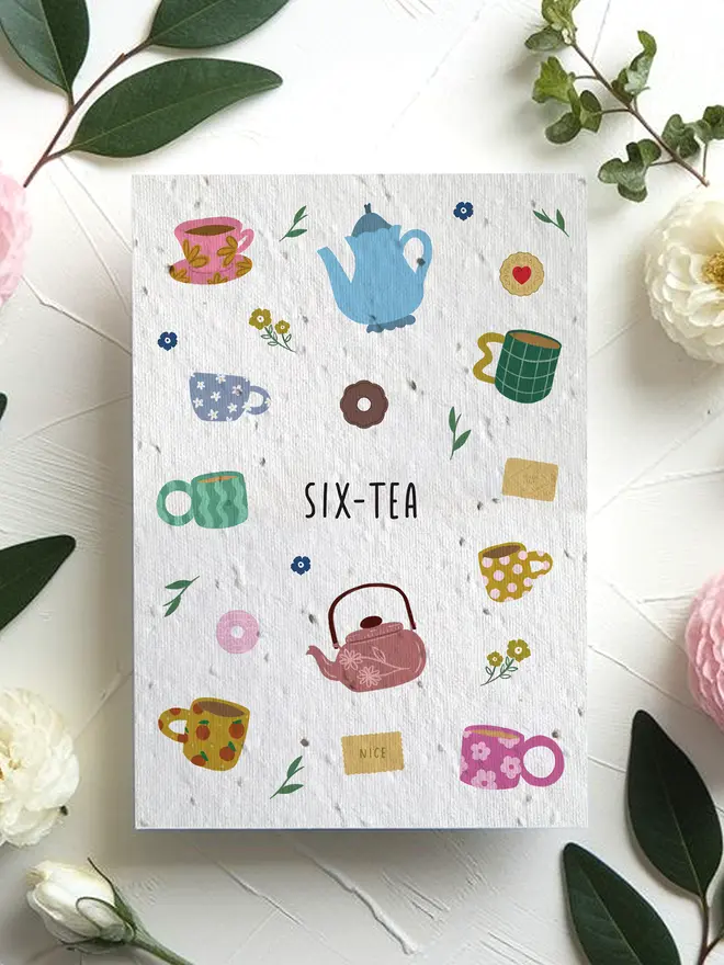 A greeting card titled “SIX-TEA” featuring colorful illustrations of teapots, mugs, tea bags, and small flowers, surrounded by pink and white blossoms with green leaves on a white textured surface.