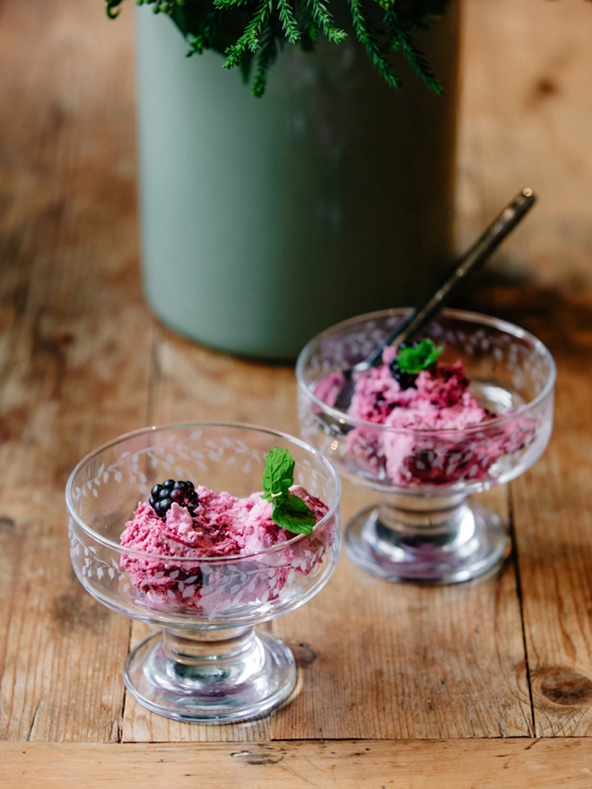 Two clear glass dessert bowls with an etched leaf pattern filled with ice cream and set on a rustic wooden table.