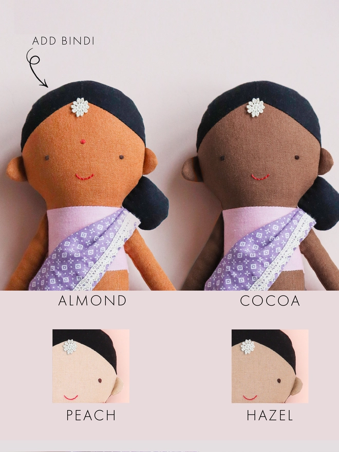 Two fabric dolls with varying skin tones, each dressed in a lavender sari with white lace. The dolls have black hair, a small white flower on their foreheads, and a red stitched smile.