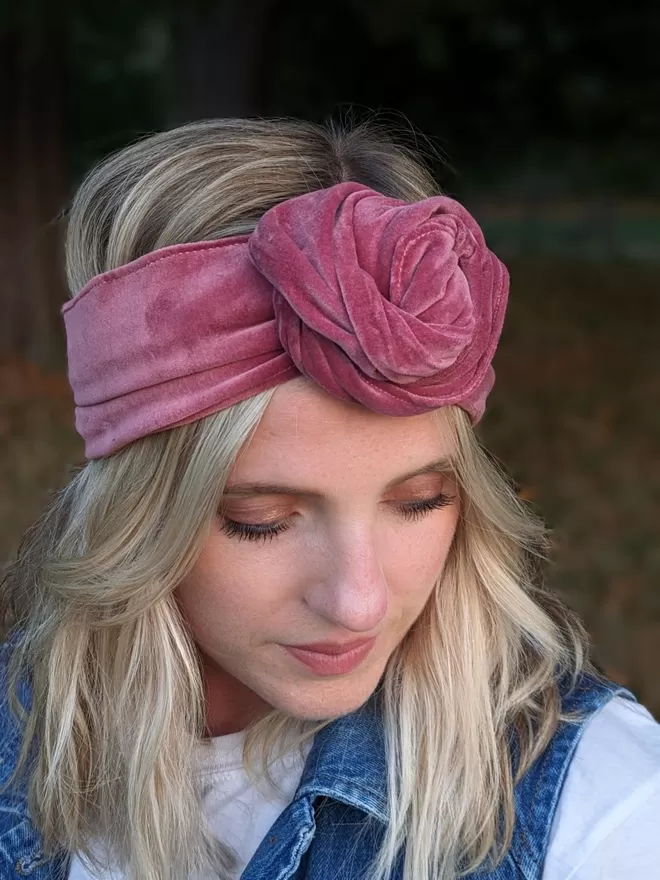 A dusty rose colour headband made from velvet fabric, tied in a rose-like knot on a blonde-haired woman.
