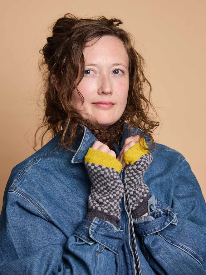 A Woman Modelling Colourful Wristwarmers In A Blue Coat In Front Of A Colourful Background