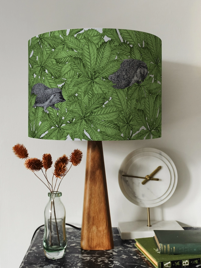 Drum Lampshade featuring hedgehogs in green leaves on a wooden base on a shelf with books and ornaments