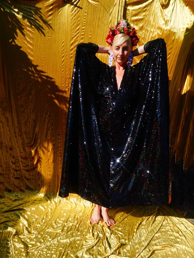 Petrol Black Holographic Sequin V-neck Kaftan Gown seen with her hands above her head.