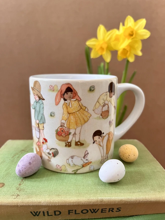 a ceramic childrens mug featuring a vinateg hand drawn easter design of little children doing easter activities, easter egg hung feeding a rabbit feeding chicks