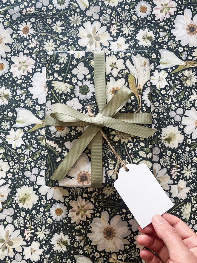 Beautiful wrapping paper and gift tag created from pressed white flowers on a black background.