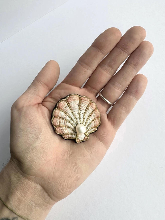 Clam shell brooch with pearl centre in the palm of a hand 