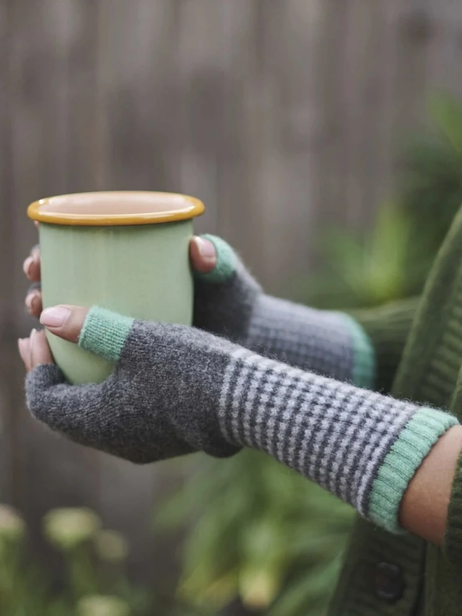 Women's Lambswool Fingerless Gloves, a woman wearing a pair of fingerless gloves holding a mug outside. 