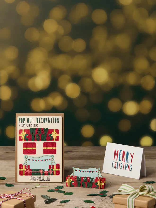 Pop out laser-cut Christmas Presents decoration and Merry Christmas card and brown kraft envelope on top of a wooden desk in front of a bokeh light effect background