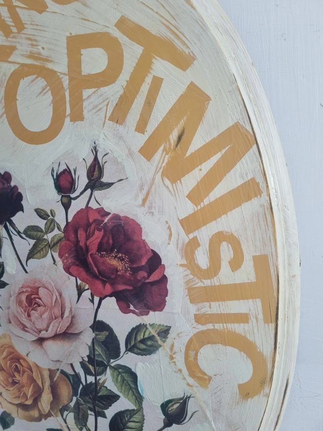 An art panel made from an upcycled table top. The image is vintage roses on a cream background with text that reads 'be fucking optimistic' in mustard yellow..