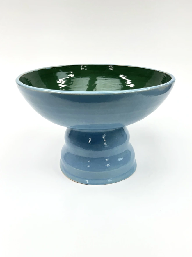 a colourful pedestal bowl with a wide shallow bowl and a chubby elevated foot. The bowl is sky blue on the outside and forest green on the inside. 