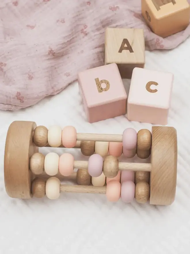 rolling wooden abacus rattle toy. a wooden rattle toy with silicone and wooden abacus beads in pink and pale colours.