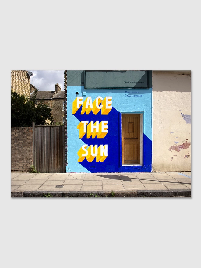 Street art painting by Survival Techniques of the words Face The Sun painted in 3d typography in yellow on a blue wall
