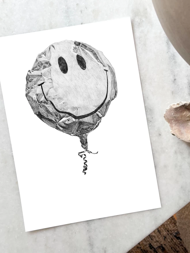 Art print of a handrawn smiley balloon laying on a table