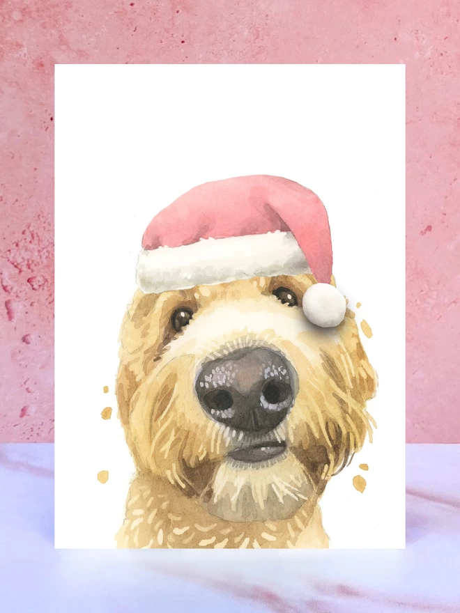 A Christmas card featuring a hand painted design of golden doodle, stood upright on a marble surface. 