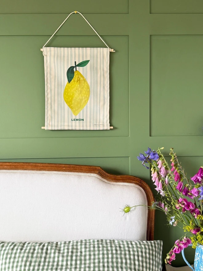 Cotton Lemon Wall Hanging, hanging on a green wall. 
