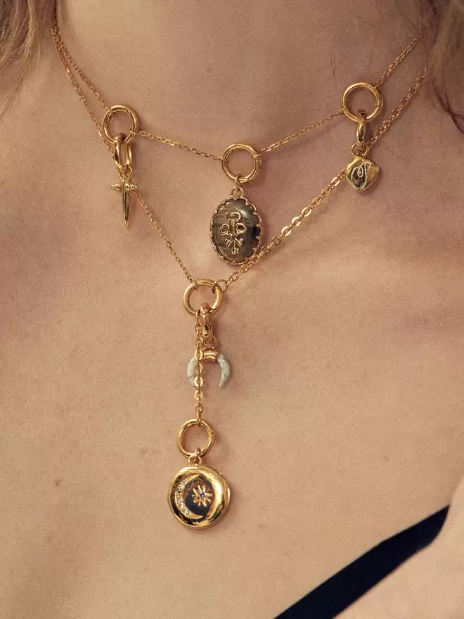 woman wearing two gold necklaces featuring a labradorite pendant, a gold locket and a mix of charms