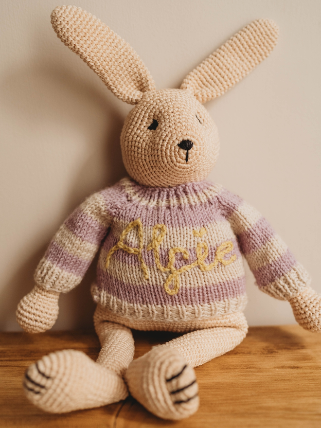 hand crochet bunny rabbit with personalised hand knit purple and white striped jumper on wooden shelf