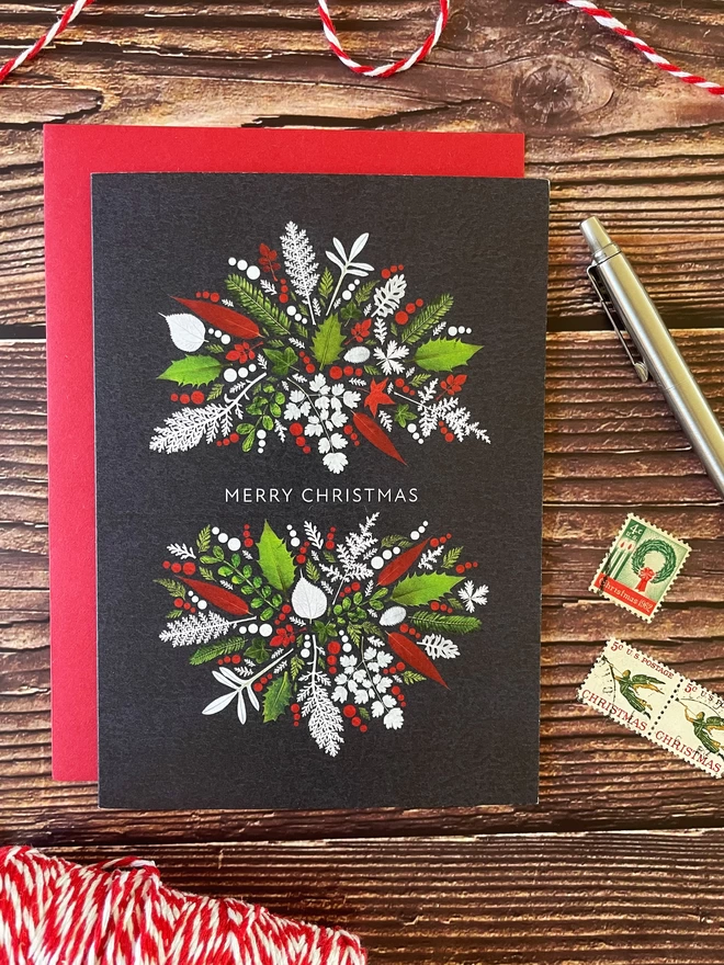 Christmas card with red, green, and white Winter leaves design - blank inside - wood background - vintage postage stamps, red and white string, ballpoint pen